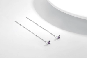 Detail of silver drop chain earrings with square purple studs on a white background