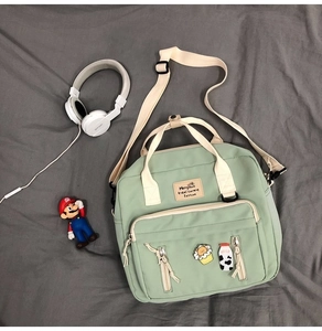 Detail view of light green canvas crossbody bag with dual handles and cartoon pins