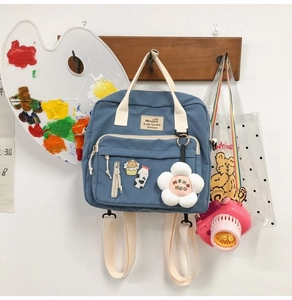 Blue canvas student bag with beige handles, front pockets and a white floral charm