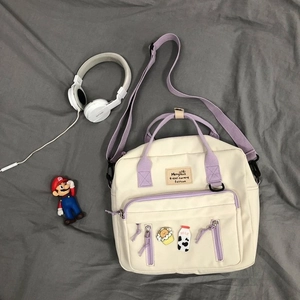 Detail of canvas crossbody bag with purple straps, milk badge, and front zipper pocket