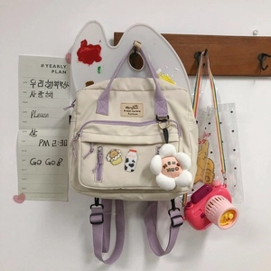 Detail of canvas backpack with floral plush pendant and cute cartoon milk bottle badge