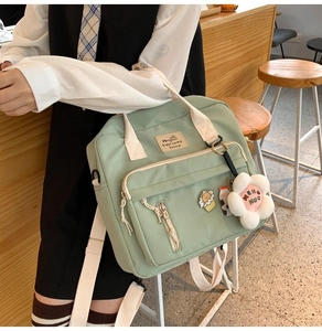 Detail of light green canvas messenger bag with cute floral pendant and cartoon badges
