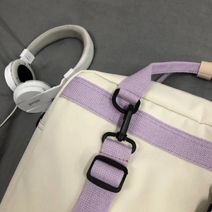 Detailed close-up of cream canvas bag with purple strap and black adjustable buckles
