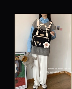 Rear view of black canvas crossbody bag with beige straps and floral charm on model