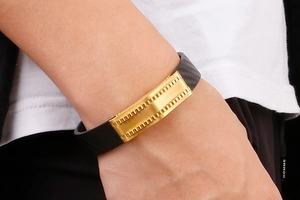 Close-up of men's black woven bracelet with golden gear-textured metal elements