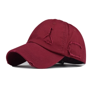 Close-up of distressed wine red cotton baseball cap with frayed brim and torn details
