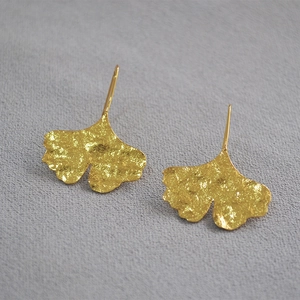 Detail of gold ginkgo leaf earrings with unique hammered texture on grey background