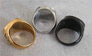 Three men's stainless steel angel rings in gold, silver, and black on a textured surface