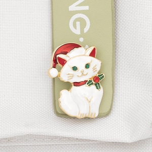 Close-up of white enamel Christmas cat brooch with red hat on green leather strap