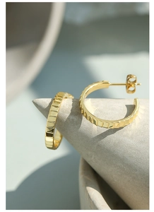 Macro detail of golden C-shaped hoop earrings featuring geometric textured metal finish