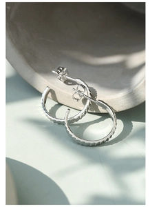 Macro detail of silver hoop earrings featuring a unique textured gear pattern finish