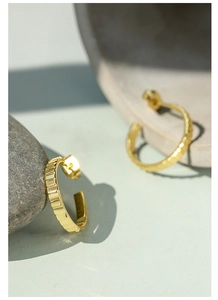 Close-up of golden textured C-shape hoop earrings on a natural stone background
