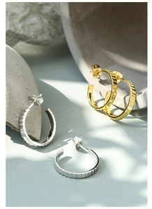 Detail showing gold and silver C-shaped hoop earrings with square textured design