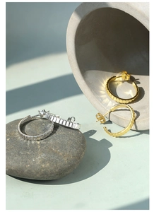 Detailed view of textured gold and silver C-shaped hoop earrings on stone display