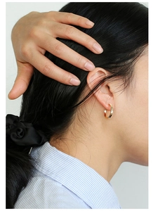 Macro view of gold C-shaped textured hoop earrings worn by a model in soft lighting