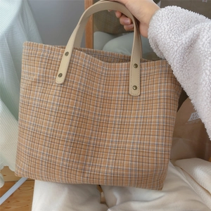 Macro detail of plaid tote bag showing canvas texture and reinforced leather handles