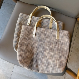 Detail of brown plaid tote bag featuring cream leather handles and metal rivet reinforcement