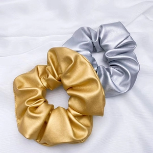Close-up of golden and silver PU leather scrunchies with metallic texture and pleats