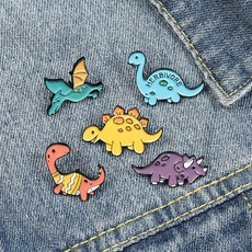Close-up of five colorful dinosaur enamel pins displayed on denim fabric background