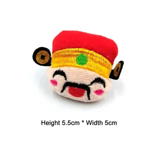 Détail d'une peluche du Dieu de la Richesse brodée, mesurant 5,5 cm de haut et 5 cm de large