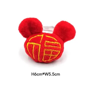Détail macro d'un accessoire en peluche rouge avec broderie Fortune jaune, 6cm x 5,5cm
