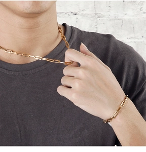 Detail of a golden paperclip chain necklace and bracelet set worn by a male model