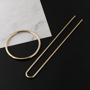 Golden U-shaped hair pin and circular hair tie set on a modern marble background