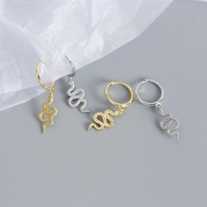 Detail of gold and silver snake hoop earrings on silk fabric showcasing luxury metal texture