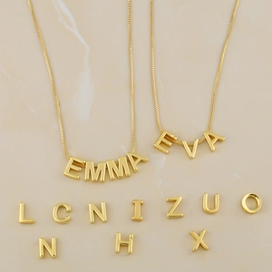 Detailed macro view of personalized golden letter pendants and initial necklaces on marble