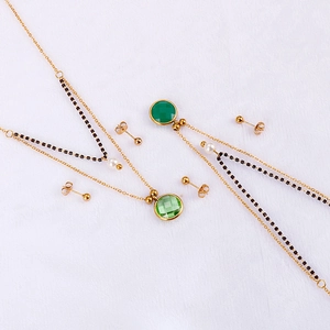 Double-layered golden necklaces and stud earrings with green gemstones on white fabric