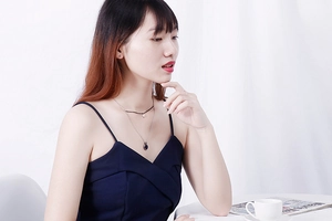 Model wearing a layered silver-toned necklace set with dark beads and oval pendant