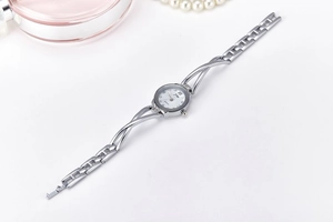 Detail of silver bracelet watch with woven metal band and white dial on a clean surface