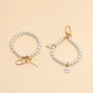 Detailed view of two pearl bead keychains with gold charms on a beige background.