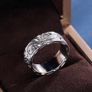 Macro shot of silver ring featuring intricate embossed floral vine patterns and glossy finish