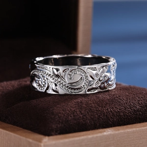Macro shot of silver ring with embossed vine pattern in a dark brown velvet jewelry box
