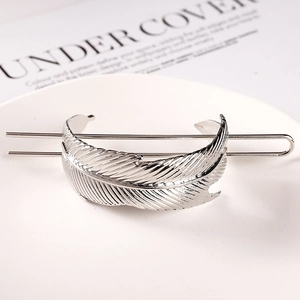Close-up of elegant silver feather metal hair pin with detailed texture on white tray