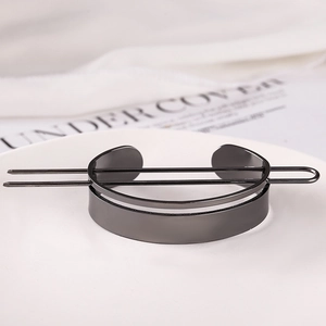 Macro view of a black metal feather hair pin and circular bun holder on a white plate