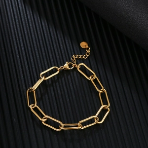 Detailed view of golden paperclip link chain bracelet with small round pendant on black