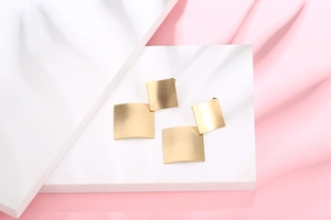Macro shot of geometric square earrings with matte brushed champagne gold finish detail