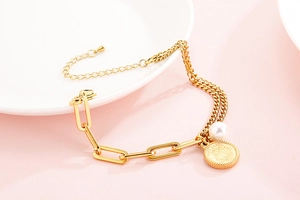 Detail of gold double-layer bracelet with pearl and coin pendant on pink surface
