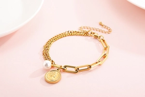 Detail of gold coin bracelet with Elizabeth II charm and white pearl on pink background