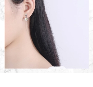 Close-up of model wearing small daisy stud earrings with white petals and yellow centers