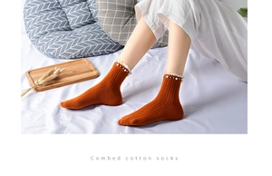 Detail of orange combed cotton sock featuring delicate lace trim and pearl accents