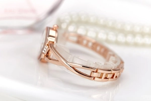 Close-up of elegant rose gold women's watch with crystal-embellished bezel on white surface