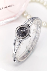 Detailed close-up of a silver bangle watch with black dial and rhinestones on white backdrop