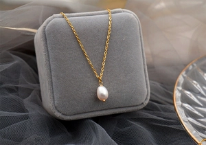 Close-up of a white teardrop pearl necklace with a gold chain on a grey velvet jewelry box
