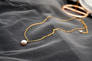 Detailed close-up of a drop pearl pendant on a gold chain against dark mesh fabric