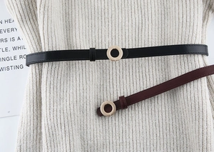 Flat lay of slim black and brown faux leather belts with minimalist gold round buckles