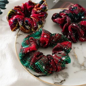 Three Christmas scrunchies with red and green plaid patterns on a marble tray