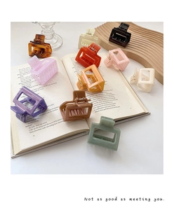 Square acrylic hair claws in assorted colors scattered on a book in a soft light setting